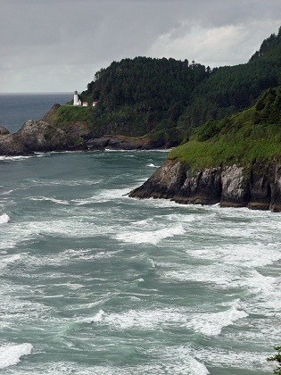 gray wavy water of the Oregon Coast with green mountains and a grey sky