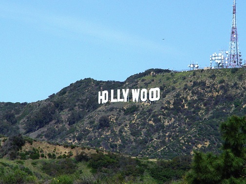 Los Angeles white Hollywood sign on the mountain with blue sky above and green trees belo